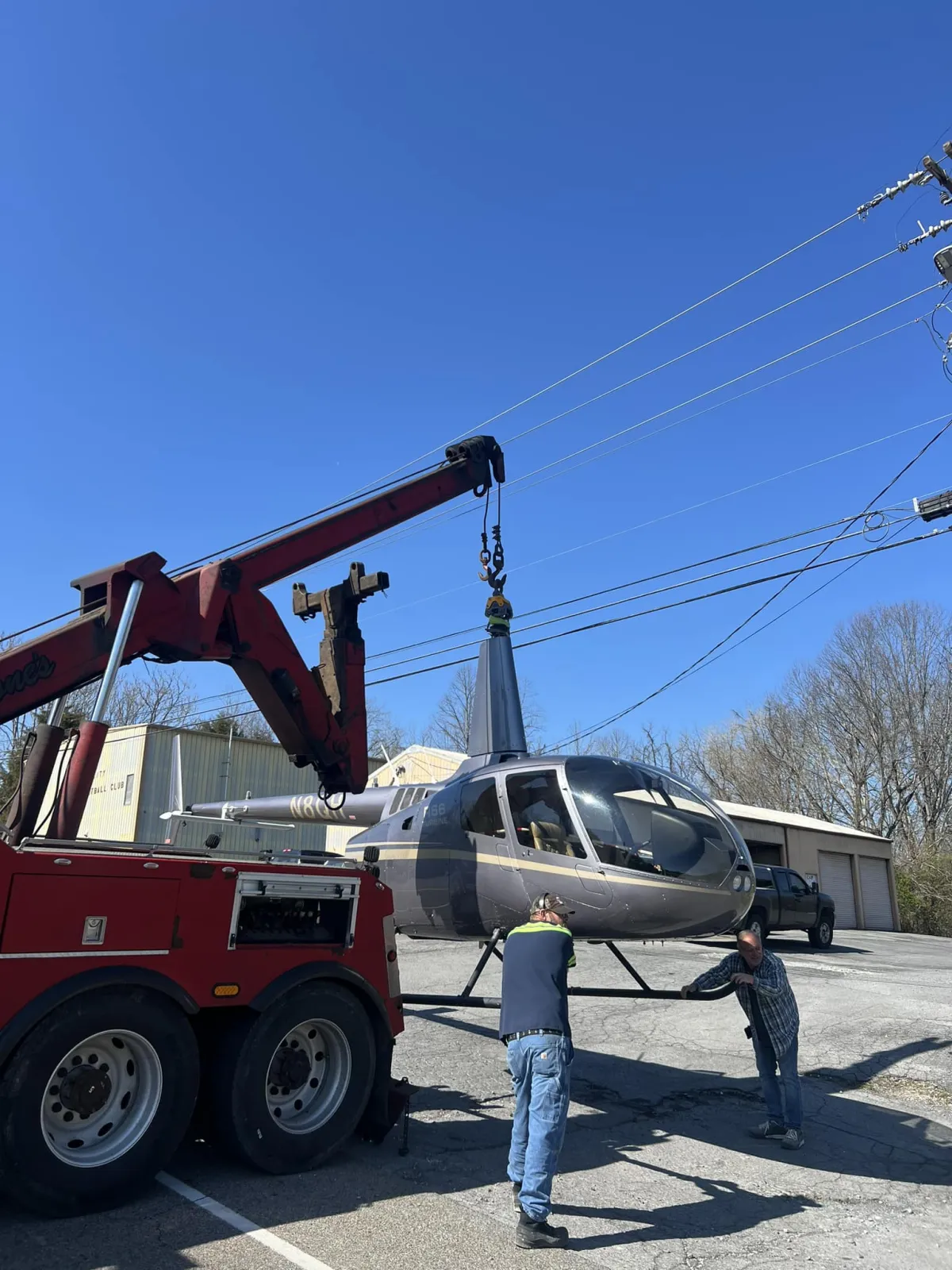 A Malone’s rotator lifting a helicopter by its mast while two of the crew steady it.