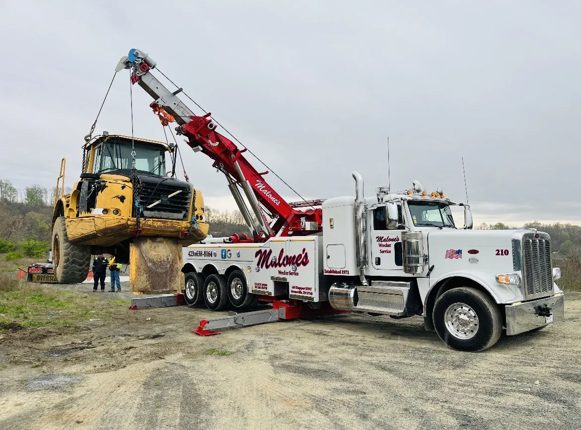 A white Malone’s Peterbilt rotator with a red boom lifting a yellow articulated dump truck.