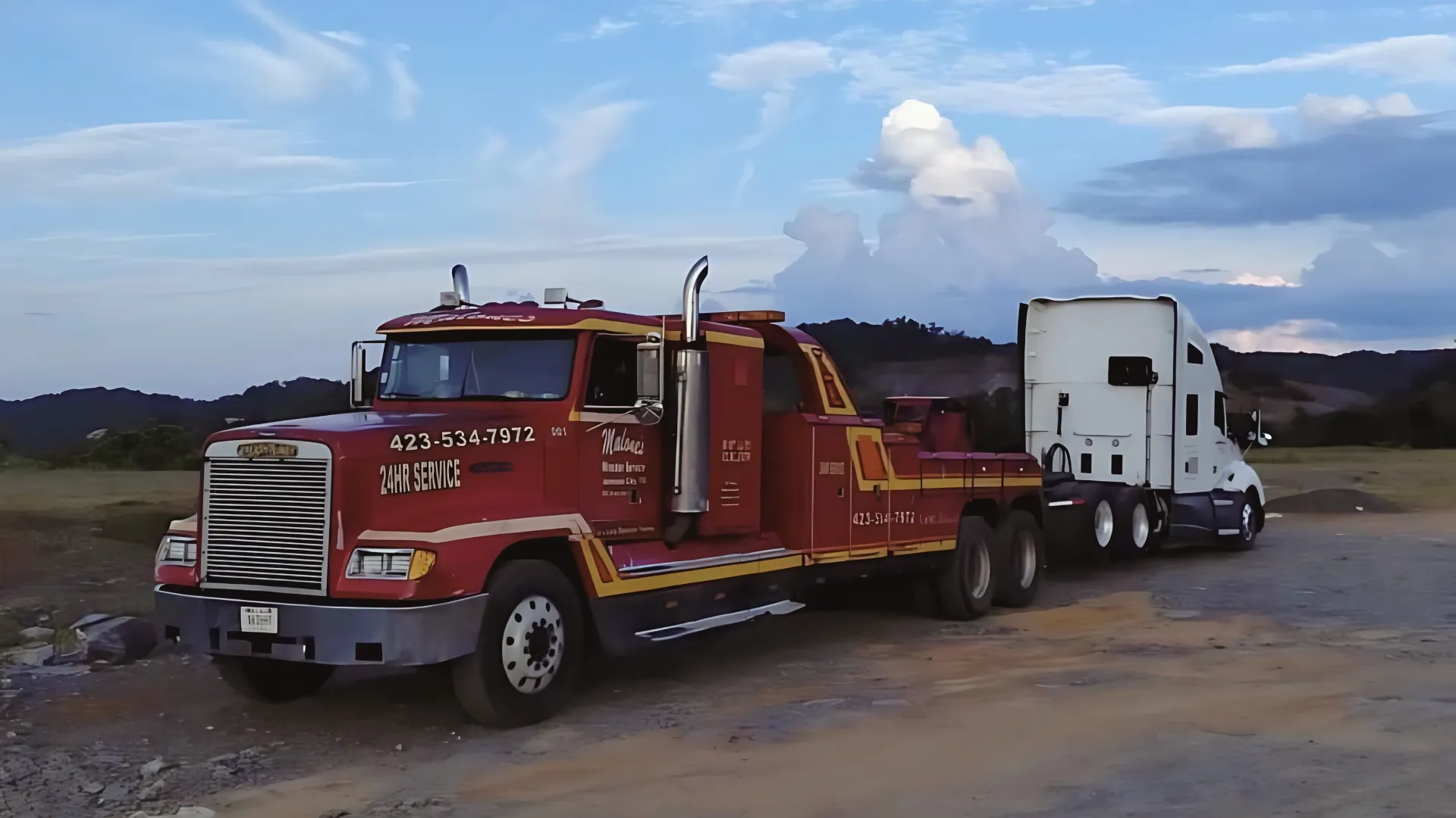 A red Malone’s wrecker with 423-534-7972 and 24HR SERVICE painted on the hood, towing a white tractor.
